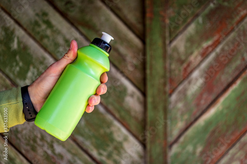 Hand of young man holding green sport water bottle or travel flask.