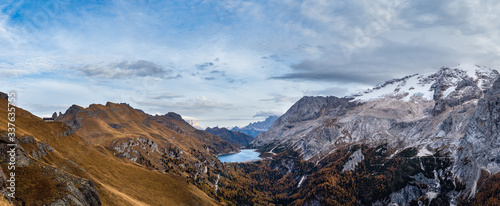 Autumn Dolomites mountain scene from hiking path betwen Pordoi Pass and Fedaia Lake, Italy. Snowy Marmolada Glacier and Fedaia Lake in far.