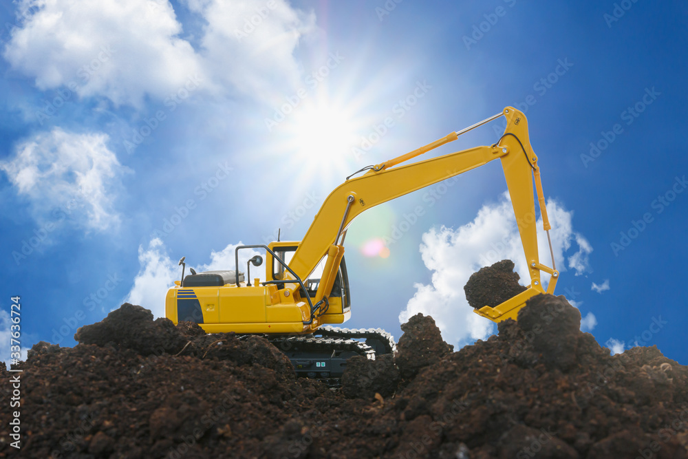 Yellow excavators are digging the soil in the construction site on the sky and sunbeam background Yellow excavators are digging the soil in the construction site on the sky and sunbeam background