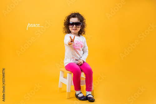 Little girl shows two fingers, gesture of peace on a yellow background