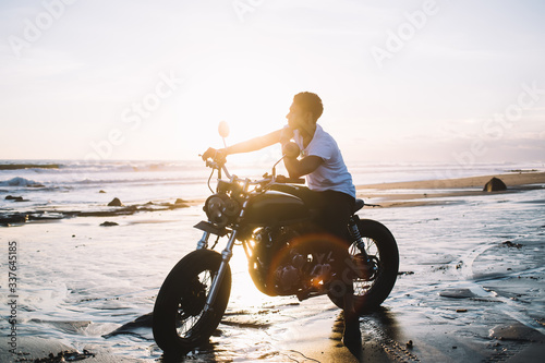 Dreaming man sitting on motorbike on sea shore during sunrise