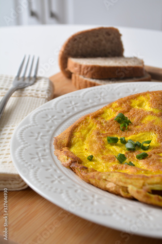 Fluffy breakfast omelette with green spring onions and fresh toast bread on a wooden surface with a napkin and metal fork
