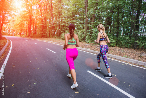 Two athletes at sunrise, running along the asphalt road through the forest. Morning fitness, jogging in the fresh air, sporty sunny day.
