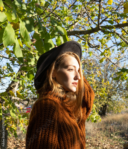 portrait of a blonde girl in a sweater and black hat on a tree background