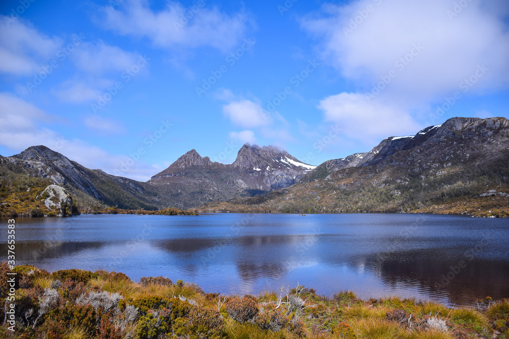 The dry grass field with the lake, snow mountain and cloudy blue sky background on sunny day in Tasmania, Australia