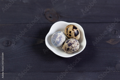 Three quail eggs in white bowl on black wooden background