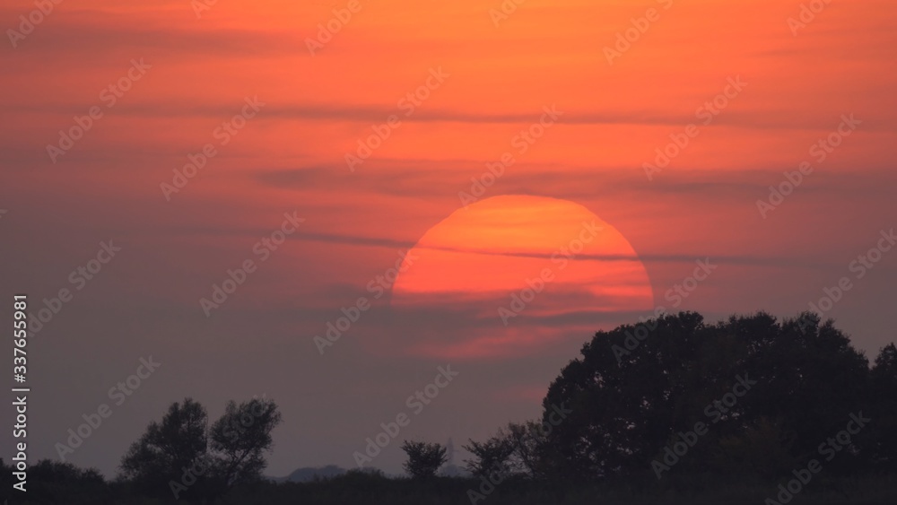 Big red sun over the meadow with trees, breathtaking sunset, Hungary