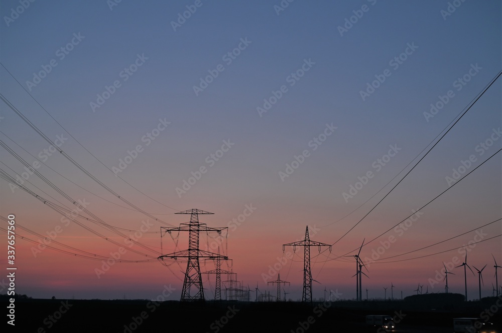 Strommasten einer Stromstrasse mit perspektivisch verlaufenden Stromkabeln bei Abenddämmerung mit rotem Himmel