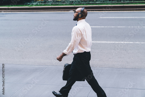 Formal man holding bag wearing headphones on street