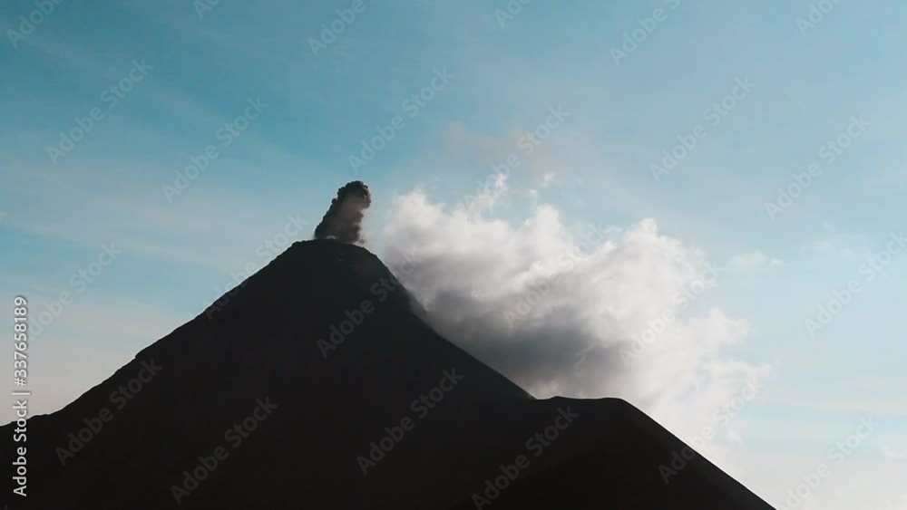 Silhouette of a volcano erupting on a sunny day