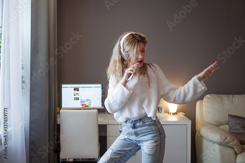 cheerful girl with a phone and big headphones is dancing and singing. Holds the phone as a microphone, photo
