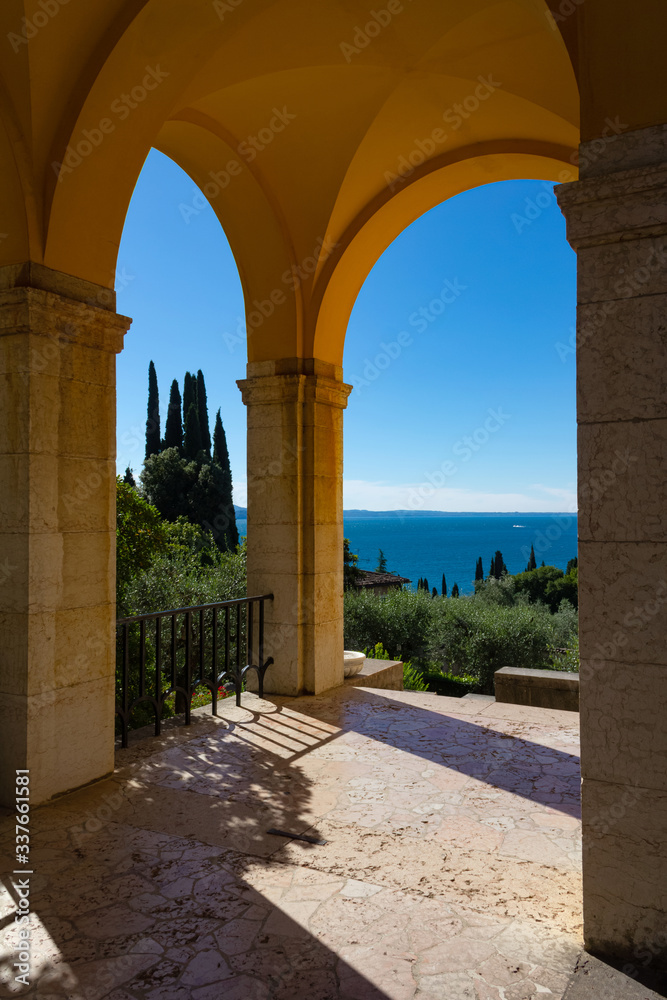 The arches of the Vittoriale degli Italiani overlook Lake Garda. The buildings are light orange and ocher, colors that create a wonderful contrast with the deep blue of the water. Gardone Riviera.