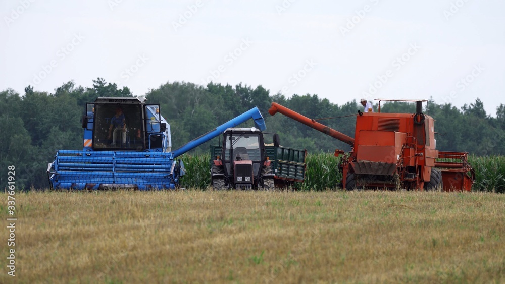 Obraz premium Tracktor and combine harvester working on the agricultural land.