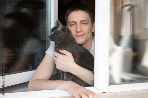 a guy with a gray cat looks out of the window