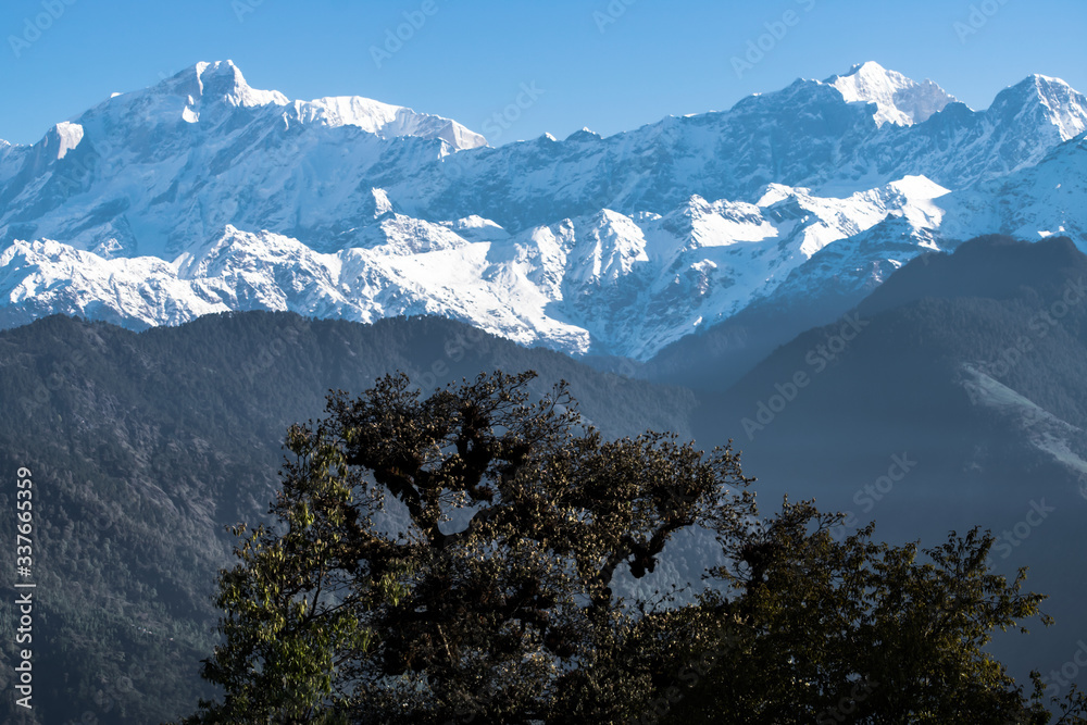 Spectacular view of snow clad mountains surrounded by forest and dramatic clouds in the sky. Amazing landscape during spring trek to Deoria lake in Uttarakhand (India).