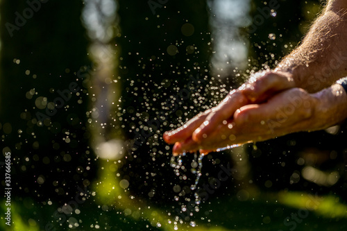 Hand of a man in the spray of water of the fountain in the summer.