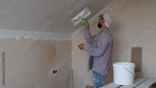 Master in a plaid shirt applying putty on putty knife and plastering a wall with finishing putty. Repair work and construction concept