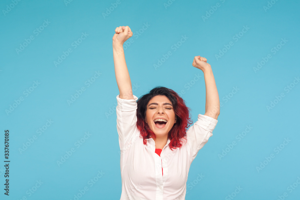 I am champion! Portrait of energetic enthusiastic woman with fancy red hair in shirt raising hands and shouting from successful winning, happy life. indoor studio shot isolated on blue background I am champion! Portrait of energetic enthusiastic woman with fancy red hair in shirt raising hands and shouting from successful winning, happy life. indoor studio shot isolated on blue background