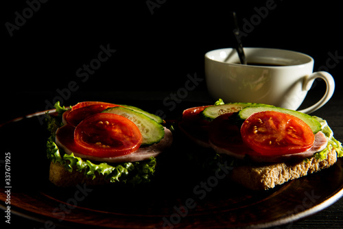 delicious sandwiches with ham, lettuce, cucumber, tomato and a Cup of coffee on a dark background.