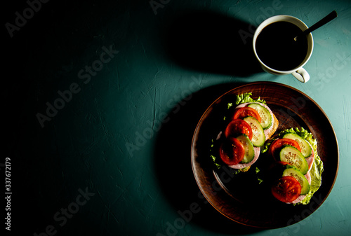 delicious sandwiches with ham, lettuce, cucumber, tomato and a Cup of coffee on a green background.