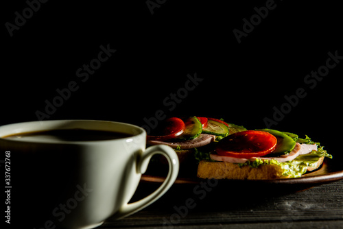 delicious sandwiches with ham, lettuce, cucumber, tomato and a Cup of coffee on a dark background.