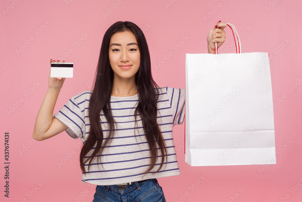 Debit card for purchases. Portrait of cheerful stylish pretty asian girl holding bank card and packages, satisfied with shopping credit, cashback. indoor studio shot, isolated on a pink background. Debit card for purchases. Portrait of cheerful stylish pretty asian girl holding bank card and packages, satisfied with shopping credit, cashback. indoor studio shot, isolated on a pink background.