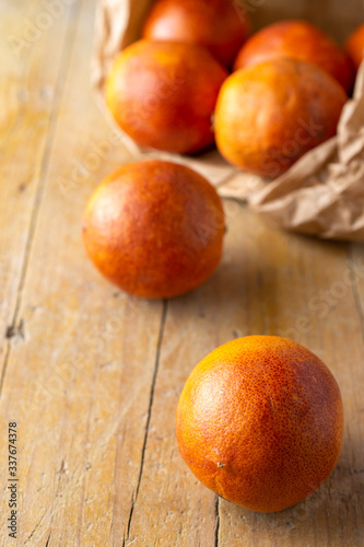 Aerial closeup of blood oranges in paper bag, with selective focus, on rustic wooden table in vertical