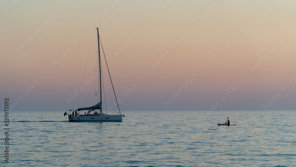 The yacht and canoeist sail on the calm sea at dusk.