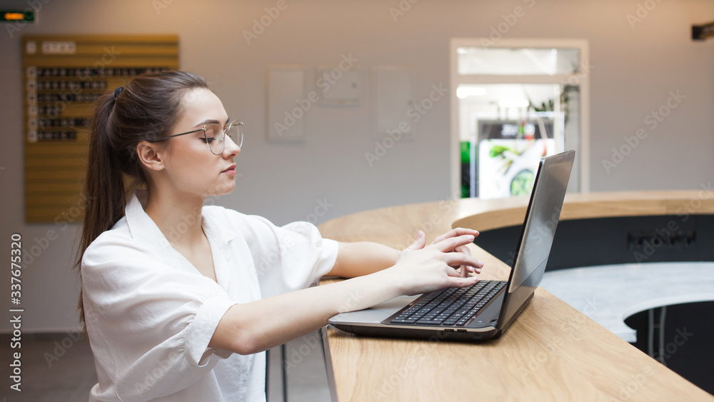 Fototapeta premium student sits at a table and uses a laptop, studying and working on the Internet.