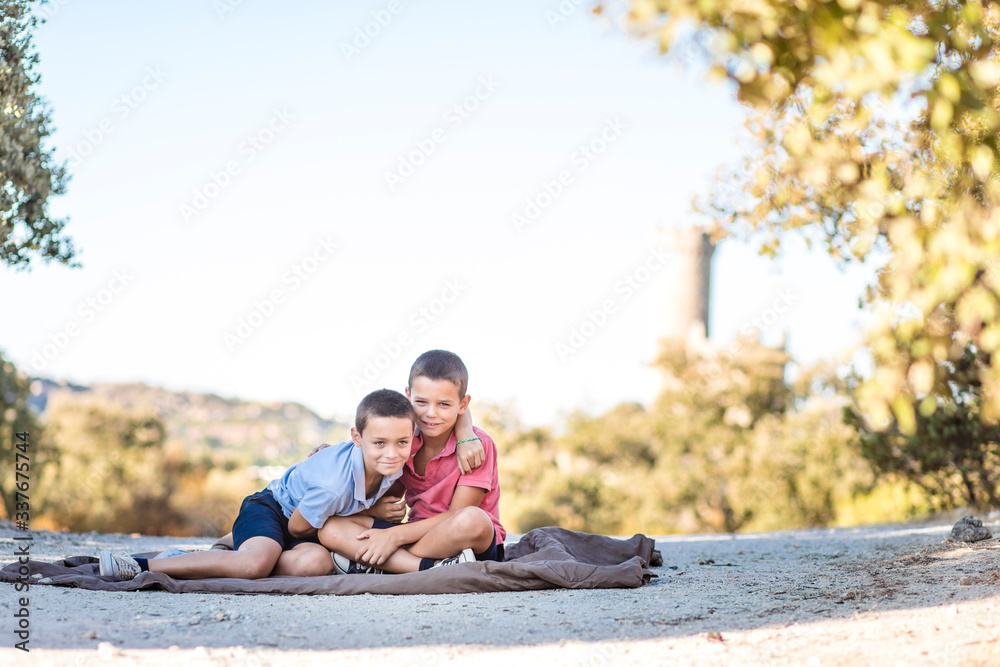 Two boys sitting on the floor in nature playing, hugging, laughing, being silly and telling each other secrets. Siblings connection.