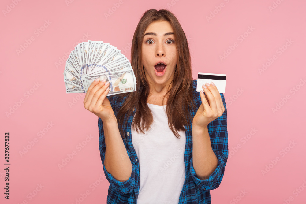 Portrait of surprised pretty girl in shirt holding credit card and dollar banknotes, surprised by lot of money, shocked by big bank loan for shopping. indoor studio shot isolated on pink background Portrait of surprised pretty girl in shirt holding credit card and dollar banknotes, surprised by lot of money, shocked by big bank loan for shopping. indoor studio shot isolated on pink background