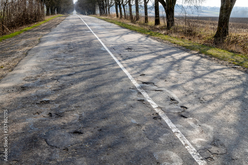 Rural countryside road damaged with winter frost. Asphalr with multiple holes and damage repaired incrementally. photo