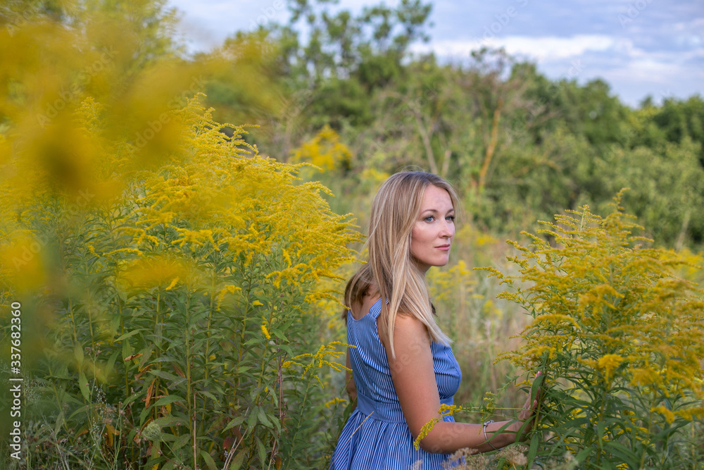 horizontal closeup portrait of a charming blonde on a background of a blooming field, sky and trees horizontal closeup portrait of a charming blonde on a background of a blooming field, sky and trees