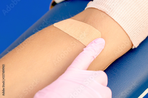 Doctor in rubber protective gloves glues an adhesive plaster on arm after blood sampling.