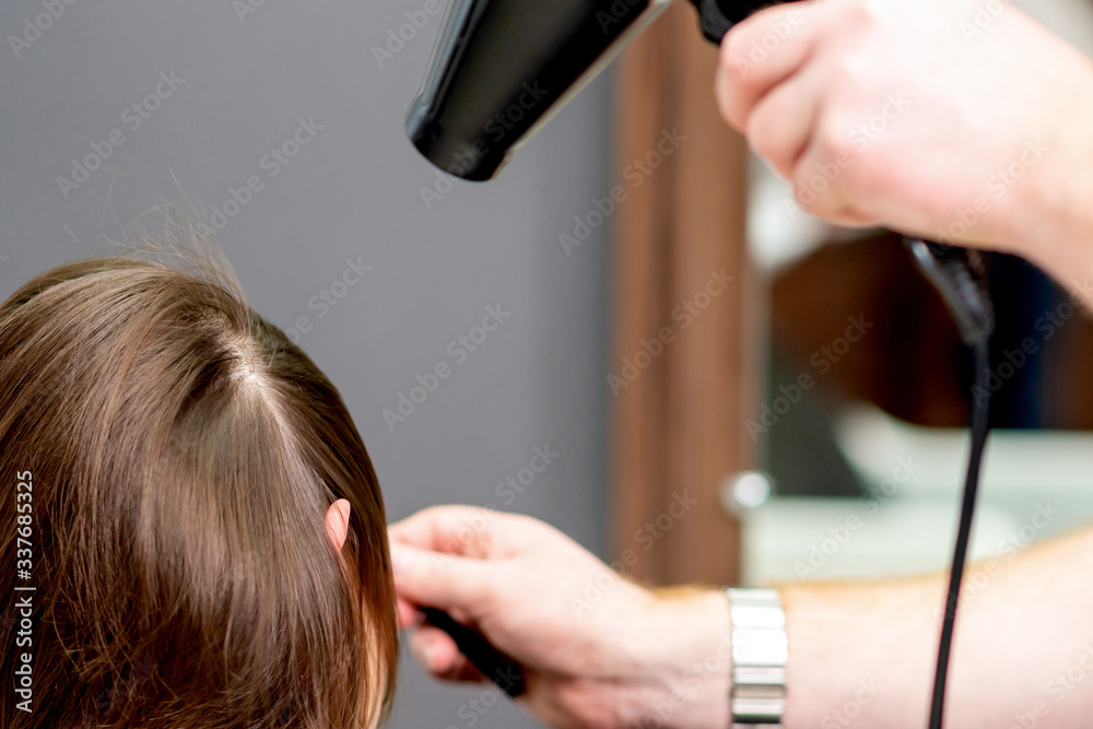 Fototapeta premium Close up of professional hairdresser is drying hair of woman back view in hair salon.