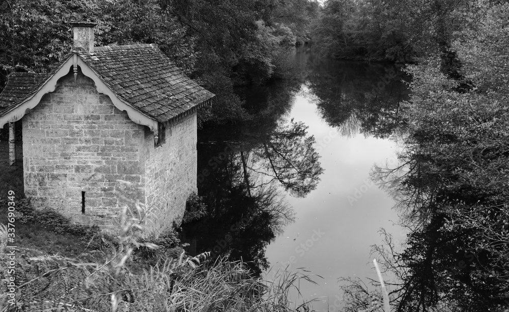 Obraz premium A monochrome image of a English boathouse and lake in the Cotswolds of England.