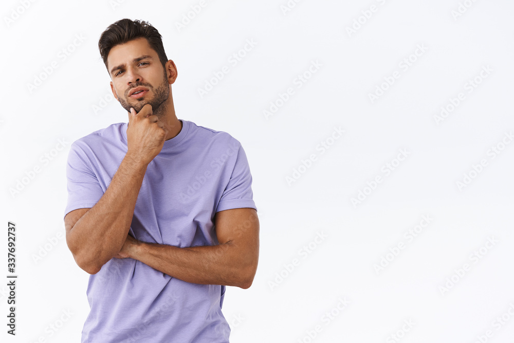 Thoughtful young man picking something in store, touching chin pensive squinting, considering what choice best, making opinion, express judgement, picking variant, pondering over white background Thoughtful young man picking something in store, touching chin pensive squinting, considering what choice best, making opinion, express judgement, picking variant, pondering over white background