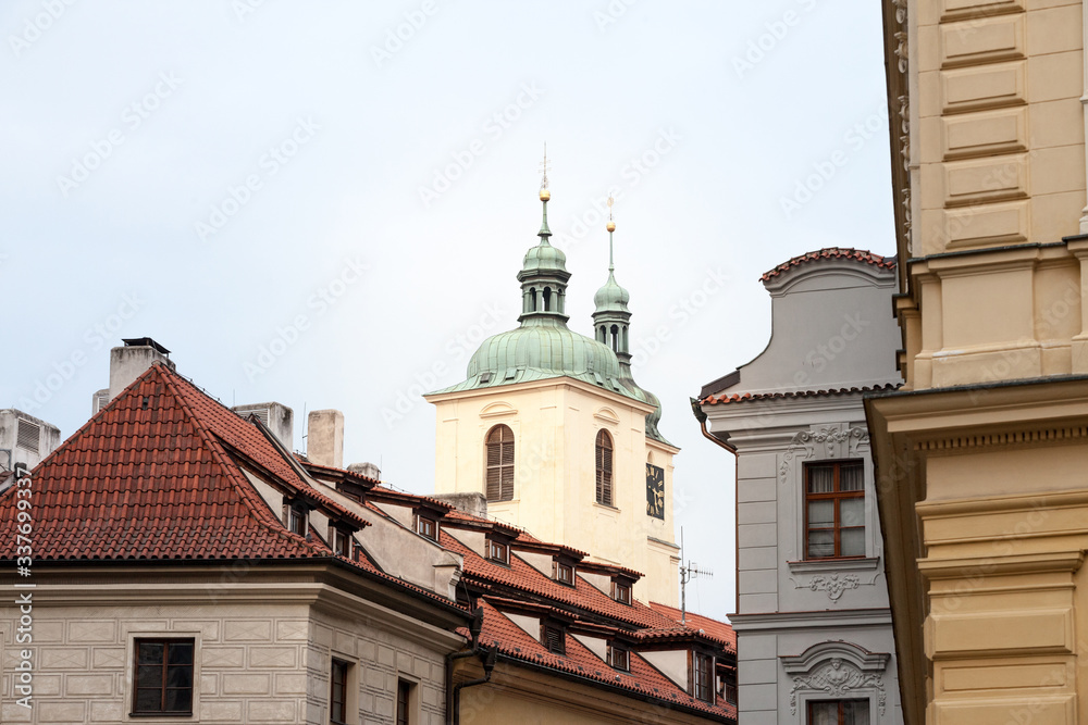Typical narrow street of Stare Mesto in the historical center of Prague, Czech Republic, with a focus on the top of the clock tower of a medieval baroque church