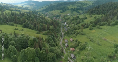 Panoramic view of Ukraine village and green forest of Carpathian Mountains in the spring. Field, white sky and beautiful green valley. Drone view from High Mountain Range. 4K video.