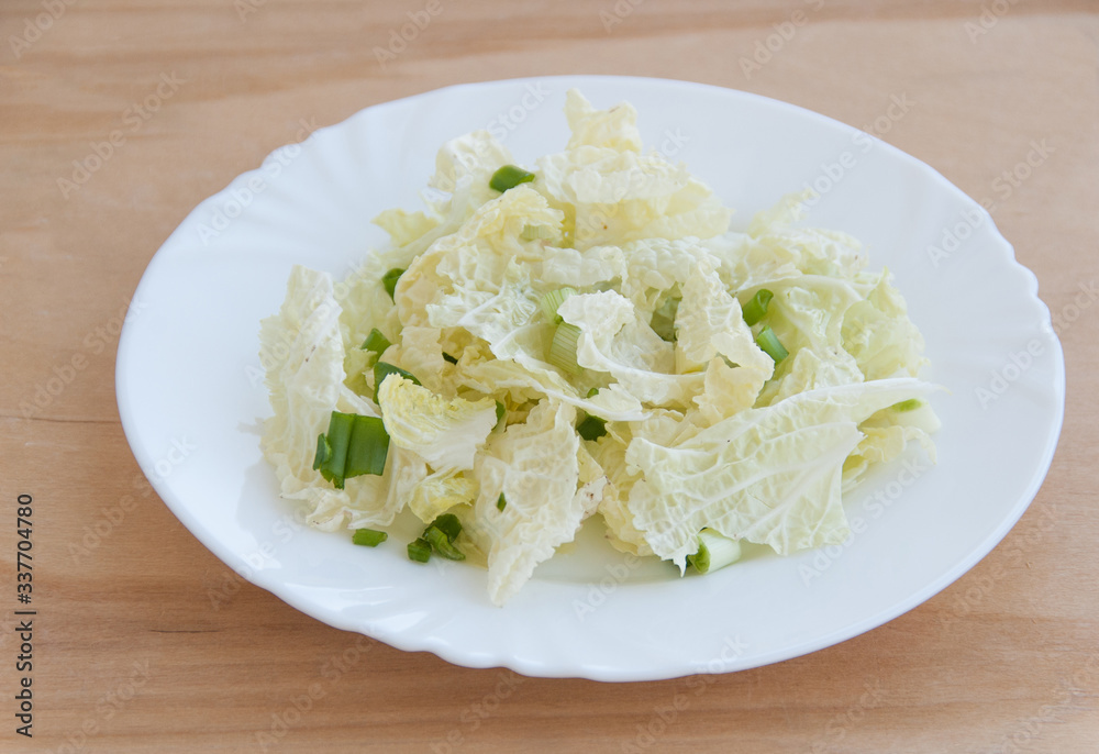 Fresh salad of green onion and chinese cabbage leaves on a white dish. Wooden table. Close-up