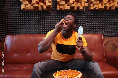 Young African-American man eating pizza. Holding a pizza knife. Copy of the space. photo