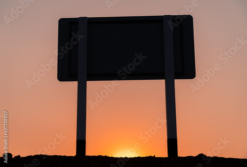 The silhouette of the signpost pass through sunlight on the roadside. During in sunset and dark color the sky.