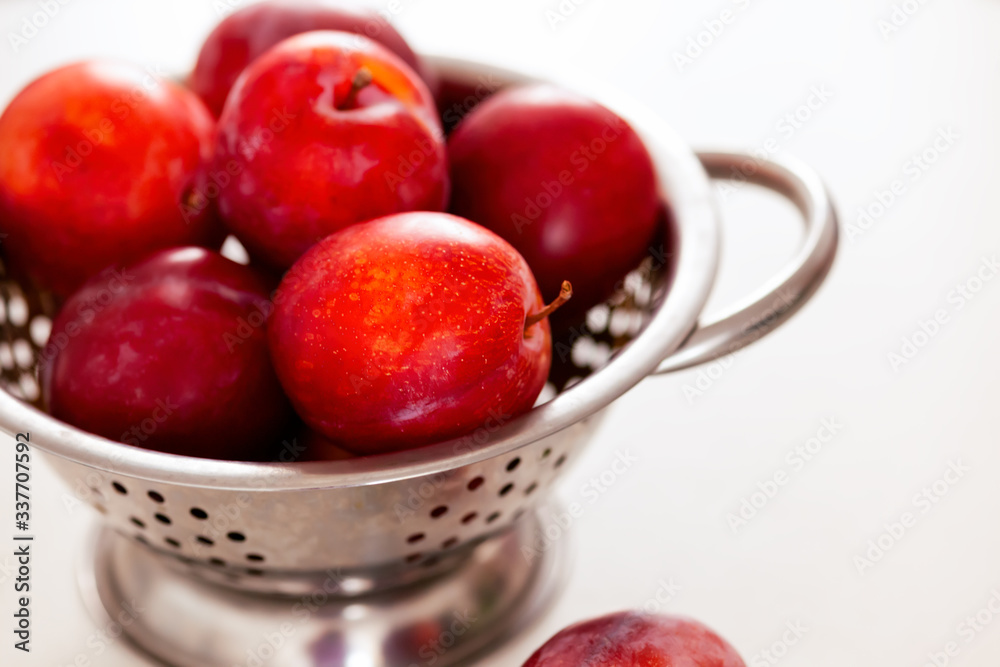 Red plums in colander. White background. Red plums in colander. White background.