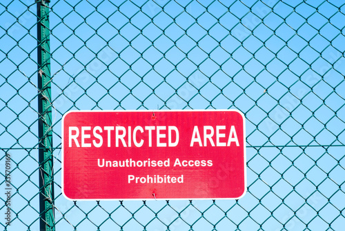 Restricted Area warning sign hanging on chain link fence outdoors against bright blue sky