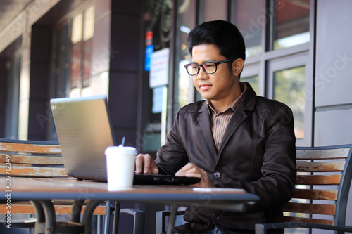  Asian businessman or student using mobile phone, laptop, tablet drinking coffee sitting on desk table, Business talk on a mobile phone