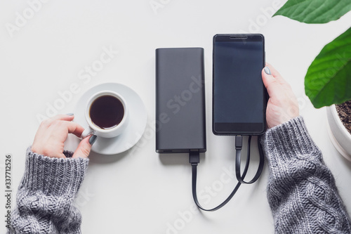 Power bank and phone on the table, top view. Charge your phone using an external battery. Modern gadgets in the hands of a woman
