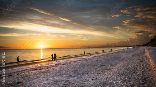 Beautiful clouds and a golden sunset light up the beach as a line of walkers enjoy the view