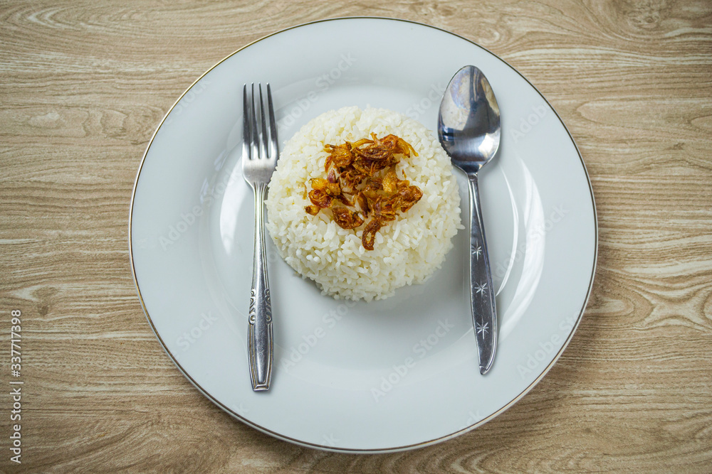 Nasi putih or white rice in white plate with fried shallot on the top.