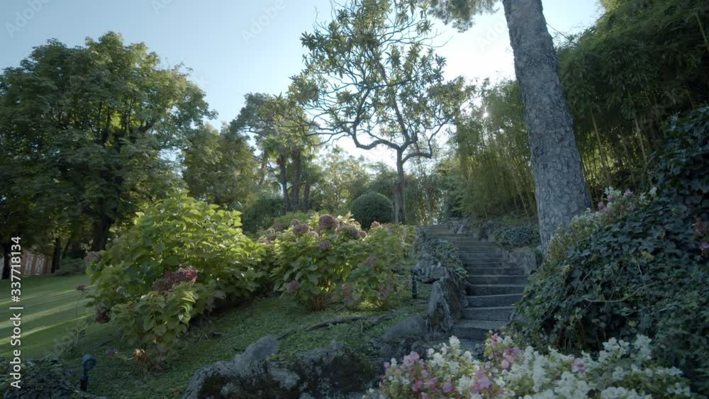 Beautiful view of a well-kept green park with flowers, a stone gray staircase on Lake Como. The bright sun shines through the trees, creating glare. Steadicam Shooting Beautiful view of a well-kept green park with flowers, a stone gray staircase on Lake Como. The bright sun shines through the trees, creating glare. Steadicam Shooting