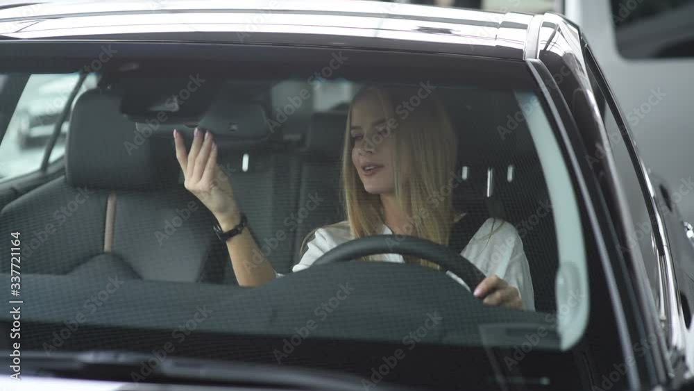 Young beautiful woman sitting in a car salon. She chooses a new car for herself. View through the windshield.